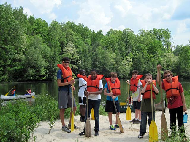 Hiram House campers wearing lifejackets preparing to row in canoes