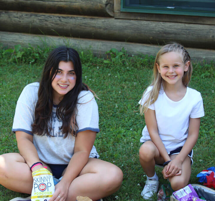 A young girl with her camp counselor eating a snack.